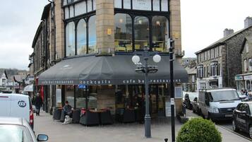 A traditional building with a cafe bar and restaurant on the ground floor, featuring large windows and a black awning.