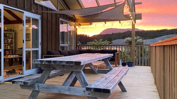 Eine Holzterrasse mit Picknicktischen und einer Sitzecke, mit Blick auf einen Sonnenuntergang und Berge in der Ferne.
