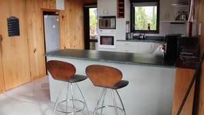 Cocina compacta con paredes de madera, una isla central con taburetes, electrodomésticos integrados y un ventanal con vistas a la vegetación.