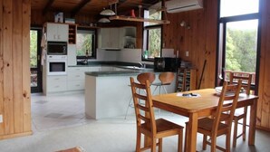 Interior de una cabaña de madera con cocina, comedor y ventanas amplias.