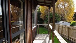 A wooden deck with a glass door leading to a backyard. - Arawa Escape - Ohakune Holiday Home (Ohakune)