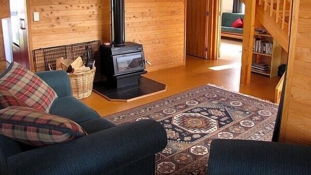 A cozy living room with a wooden interior, a fireplace, a sofa, and a staircase. - Arawa Escape - Ohakune Holiday Home (Ohakune)