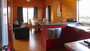 A compact kitchen with a dishwasher, a dining area with a table and chairs, and a living room with a sofa. - Arawa Escape - Ohakune Holiday Home (Ohakune)