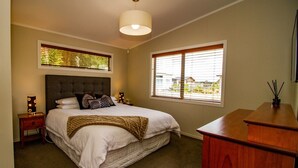 A bedroom with a large bed, bedside tables, a wooden dresser, and a window with blinds. - 1 bedroom Restful retreat w/Spa for couples (Ohakune)