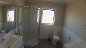 A bathroom with a glass-enclosed shower, a toilet, a sink, and a window providing natural light. - Skyline Apartments Raglan (Upper Apartment) (Raglan)