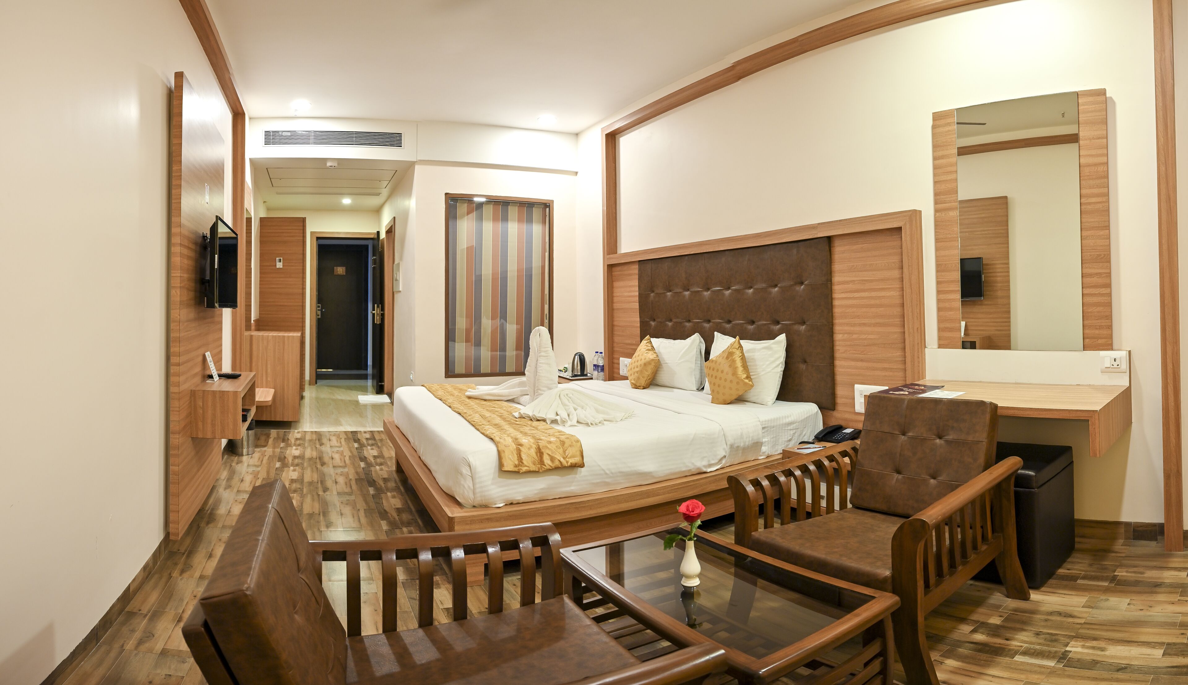 A hotel room with a bed, a desk, a chair, a mirror, and a TV.