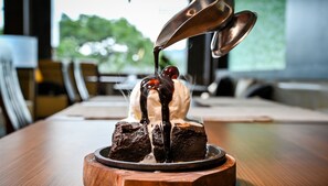 A dessert on a wooden board with a spoonful of sauce being poured over it.
