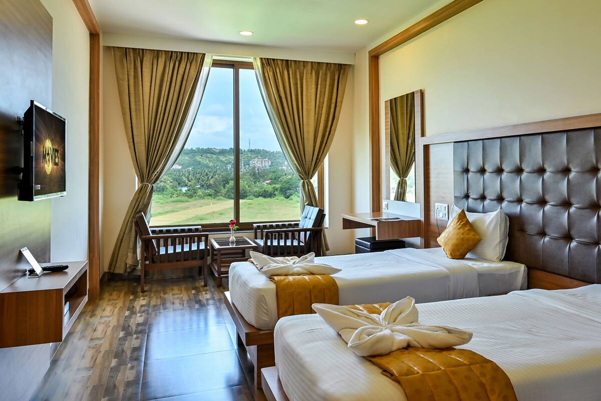A hotel room with two beds, a TV, a desk, and a view of a green landscape.