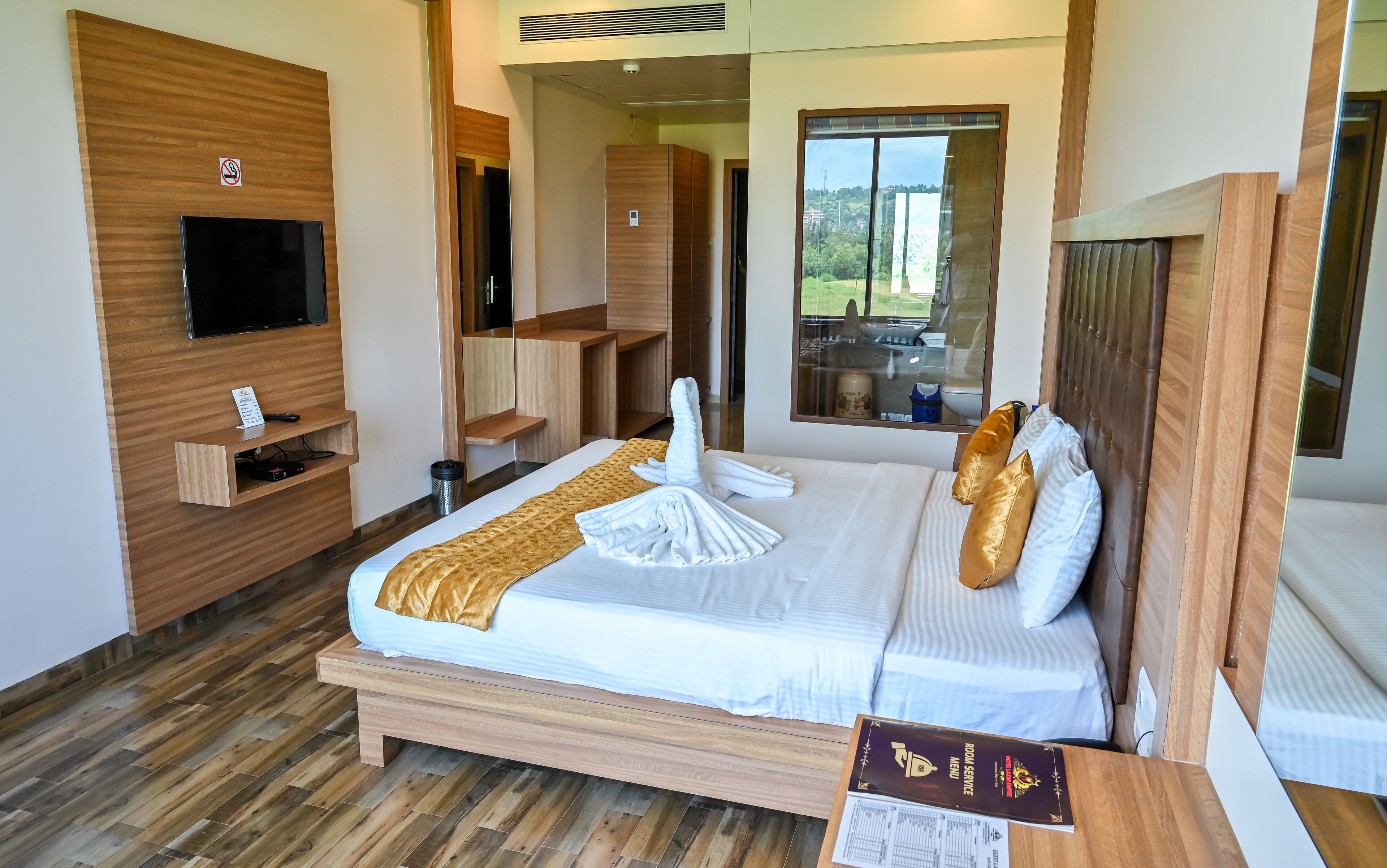 A hotel room with a bed, a TV, a wooden desk, and a window with a view.
