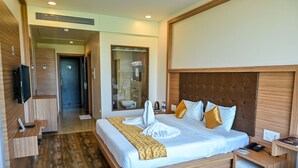 A hotel room with a large bed, wooden headboard, bedside tables, a TV, and a bathroom visible through an open door. - Hotel Laxmi Empire (Margao)