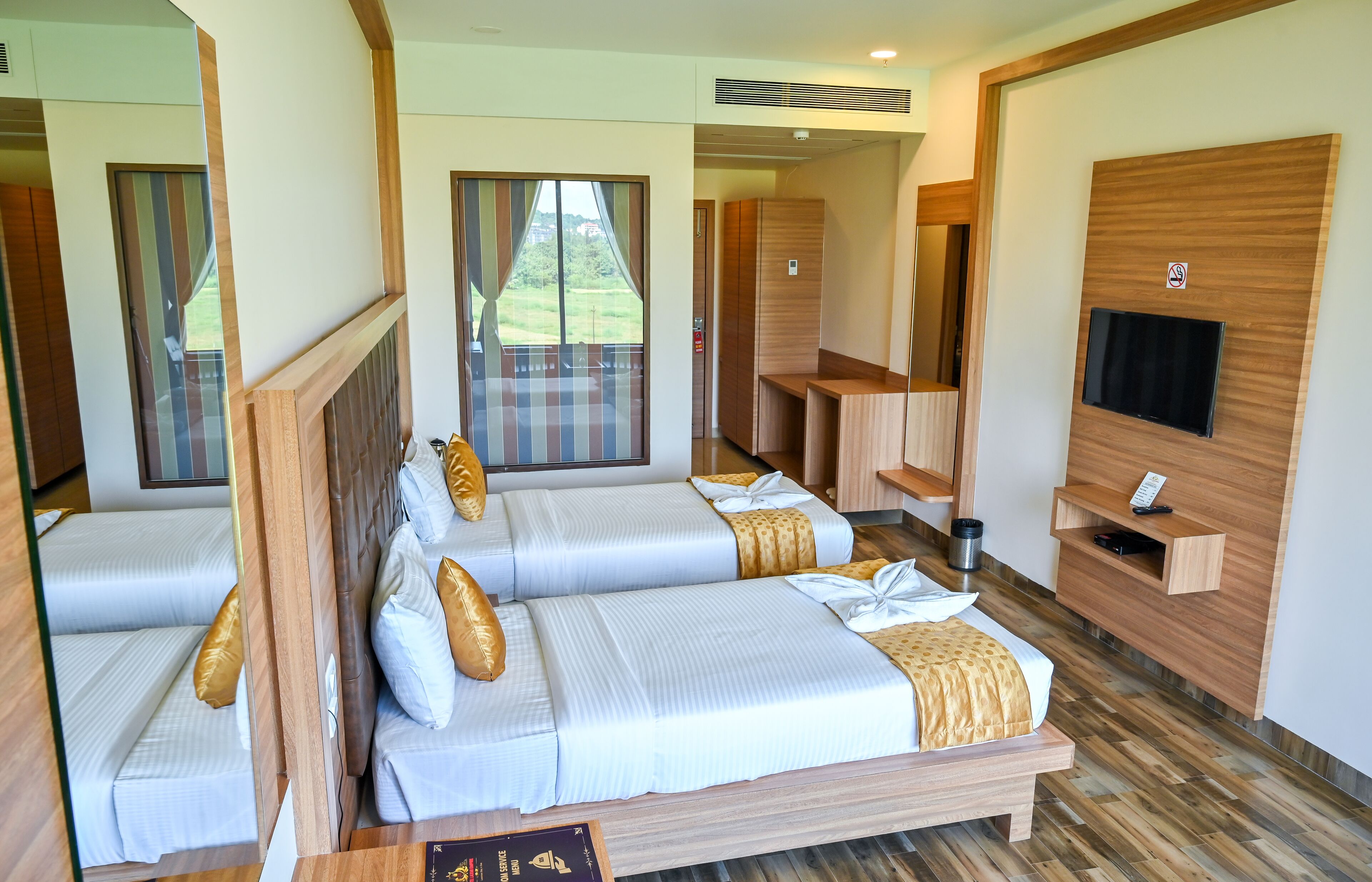 Quarto de hotel com duas camas, televisão e um armário de parede em madeira.