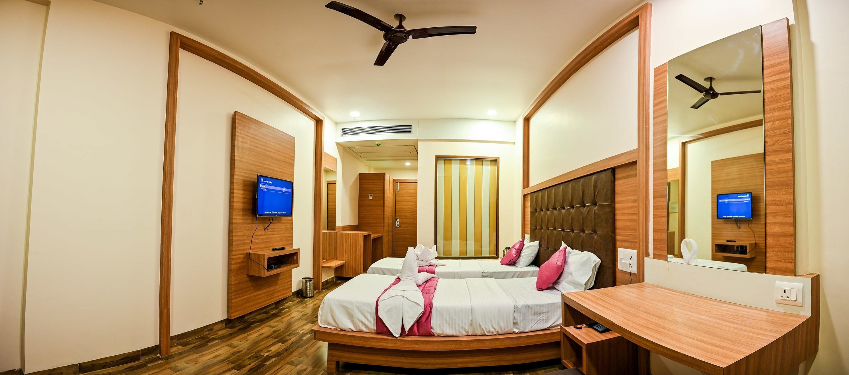 Habitación de hotel con dos camas, un escritorio, un televisor y un ventilador de techo.