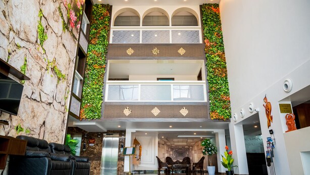 A lobby with a marble wall, a black leather sofa, a reception desk, and a check-out counter. - Hotel Laxmi Empire (Margao)