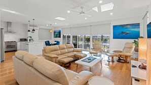 A modern living room with a beige sofa set, a coffee table, and a dining area with blue chairs. - 108 Madaffari Drive - bring your boat! (EXMOUTH)