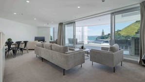 A modern living room with a sofa set, a coffee table, and a dining area with chairs and a table. - The Oceanside Belle Mt Maunganui (Mt Maunganui)