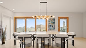 Ett modernt matområde med ett stort bord och sex stolar, stora fönster med utsikt över staden och en hängande lampa.