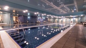 En stor inomhuspool med klart vatten, omgiven av sittområden och ett trädäck.