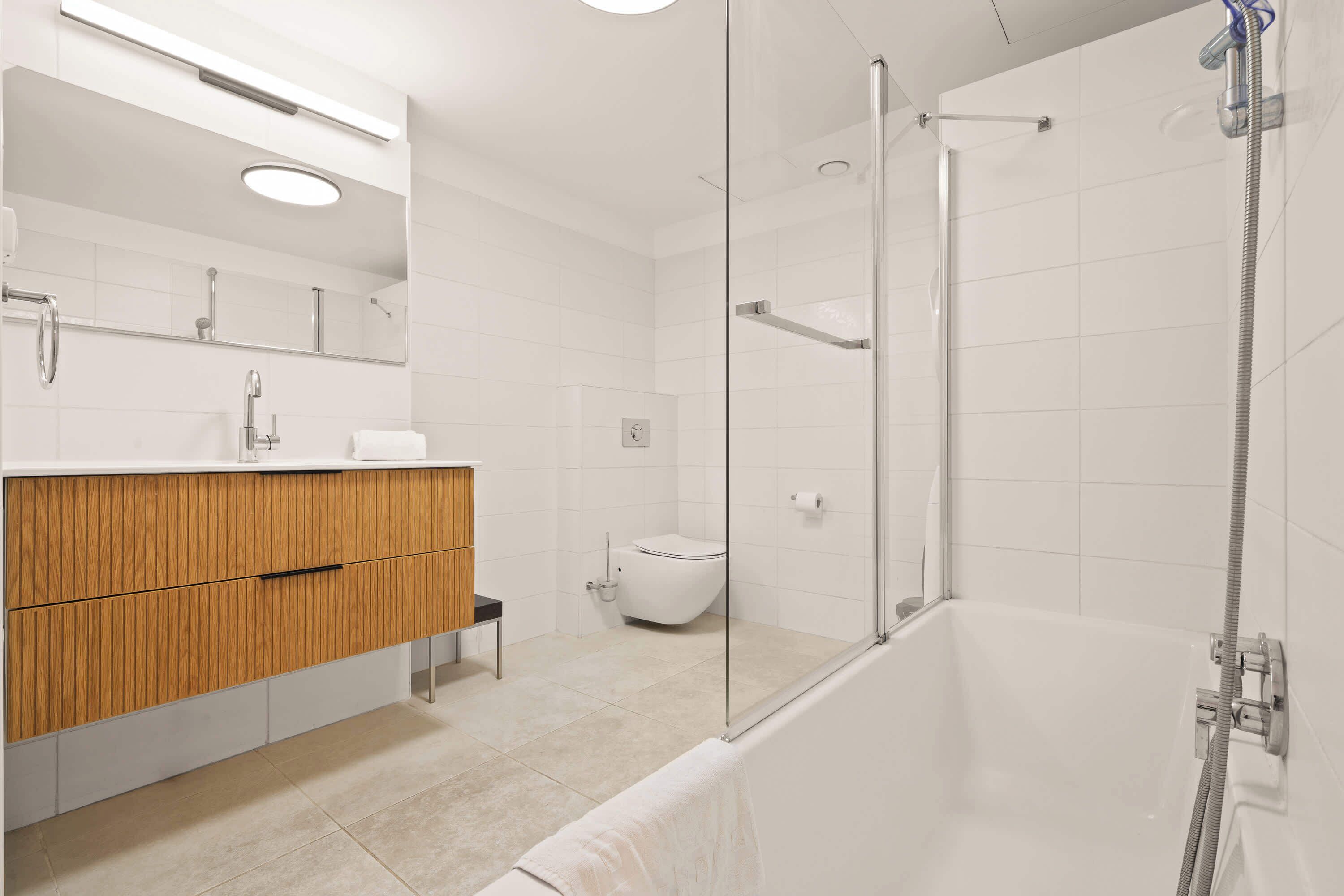 Een moderne badkamer met een douchecabine van glas, een houten wastafelmeubel en een wit toilet.