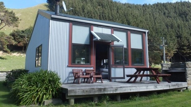 Une petite cabane à un seul étage, dotée d’une terrasse, de grandes fenêtres et d’une cheminée.