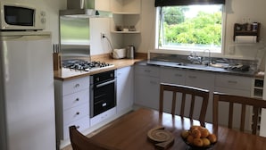 Una cocina moderna con armarios blancos, estufa a gas, microondas y ventana con vista a zonas verdes.