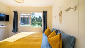 Un dormitorio con cama, cortinas, un televisor montado y una lámpara fijada a la pared.