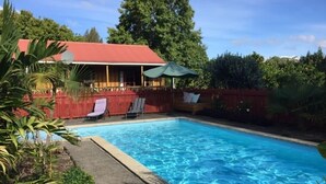 Una piscina con un edificio de techo rojo al fondo, rodeada de vegetación.
