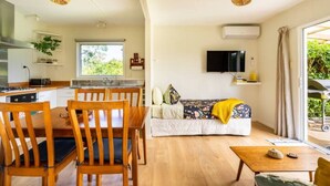Una cocina moderna con sillas de madera, una mesa de comedor, un sofá con una manta amarilla y un televisor montado en la pared.