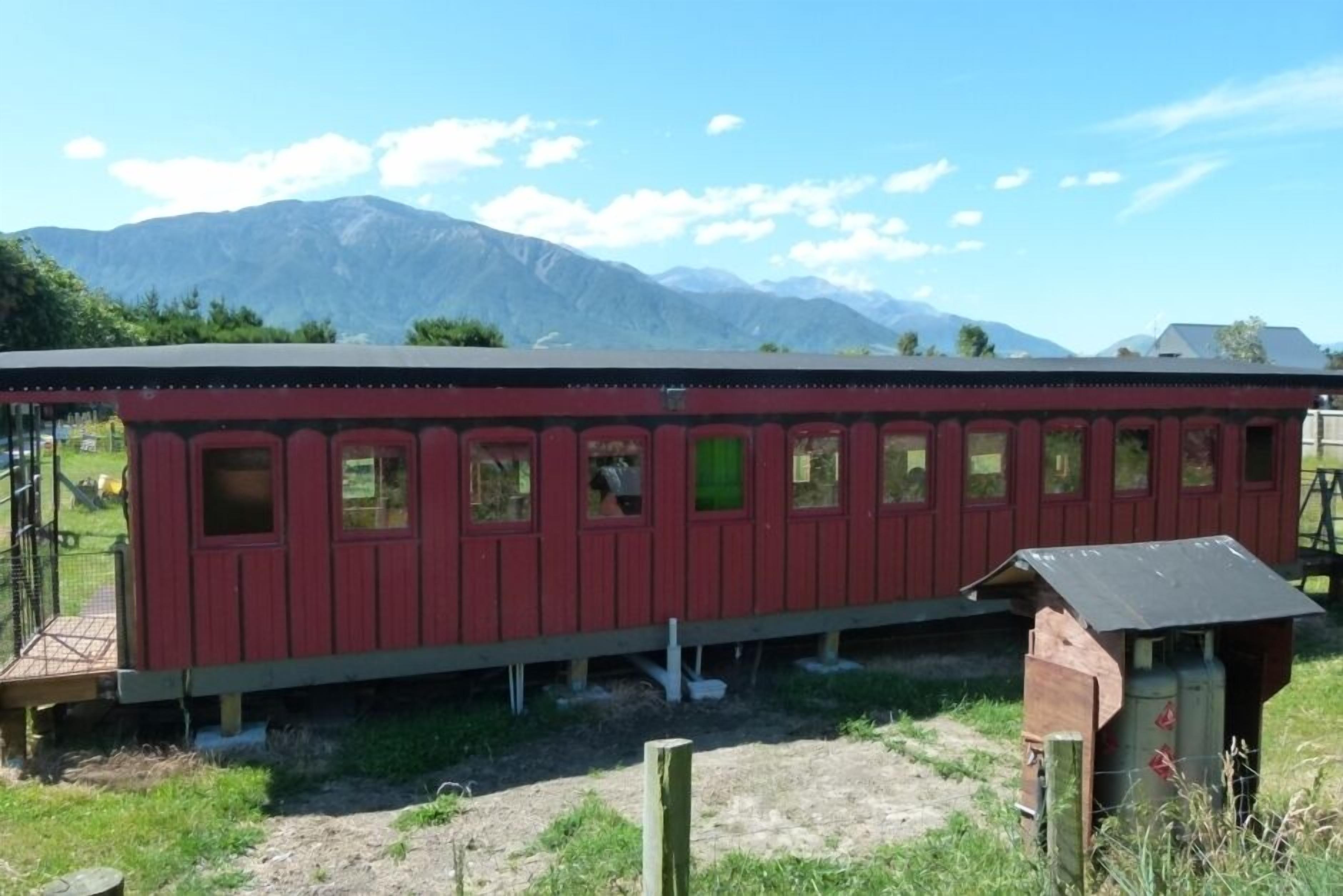 Ein roter Zugwagen mit zahlreichen Fenstern vor einer gebirgigen Kulisse.
