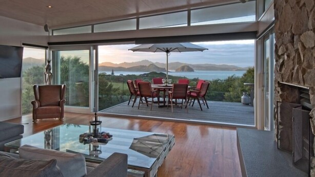 A modern living room with a glass coffee table, a sofa, and a dining area with red chairs and a table. - Barrier Headquarters entire complex. Unobstructed 270 degree view beach/mountain (Medlands Beach)