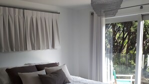 A bedroom with a large bed, a hanging light fixture, and a view of the outdoors through a sliding door. - Barrier Headquarters entire complex. Unobstructed 270 degree view beach/mountain (Medlands Beach)