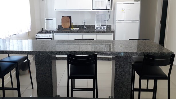 A kitchen with white cabinets, a granite countertop, a stove, a microwave, a refrigerator, and two black chairs. - 211, 2-bedroom apartment near the beach (Bombas)