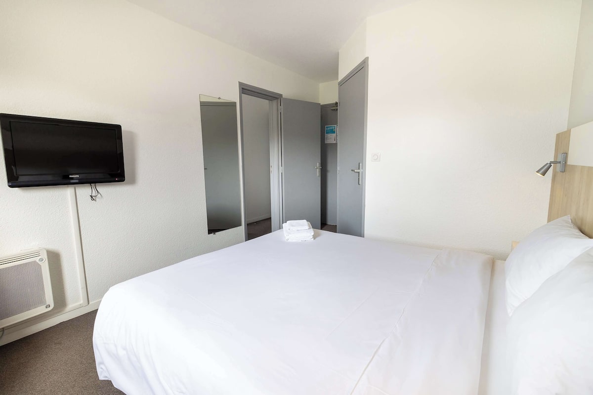 A hotel room with a bed, a flat-screen TV mounted on the wall, a mirror, and a door.