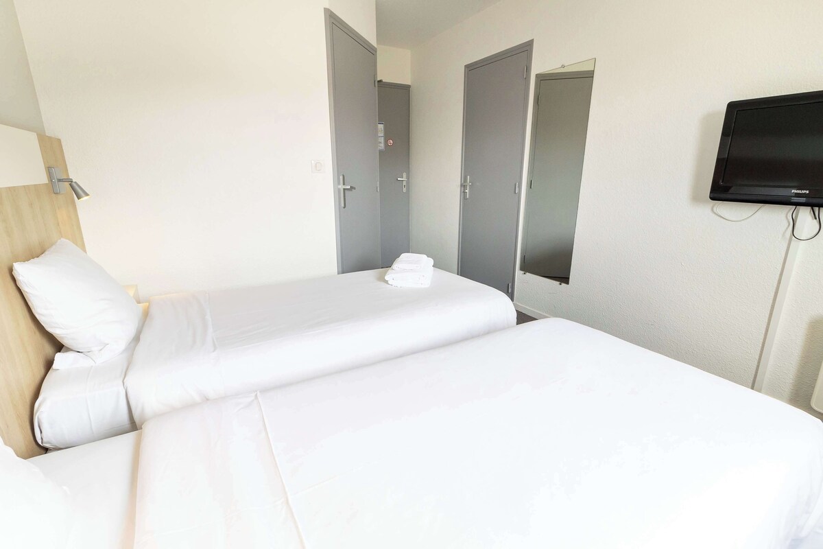 A hotel room with two beds, a flat-screen TV, and a wooden headboard.