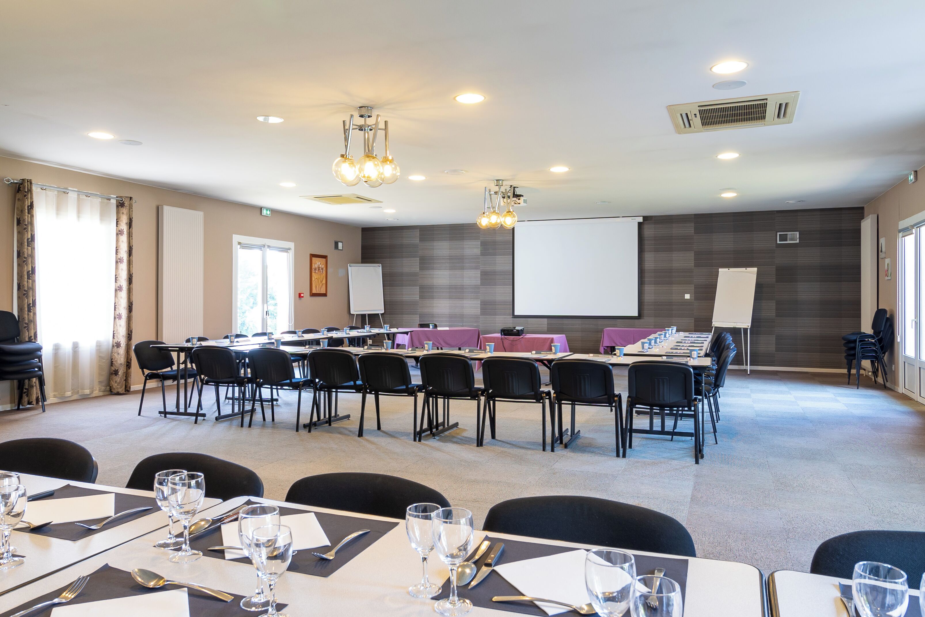 A conference room with a long table, chairs, a projector screen, and a whiteboard.