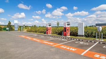 Ein Parkplatz mit Ladestationen für Elektrofahrzeuge, gekennzeichnete Stellplätze für 50 kW und 22 kW sowie ein Schild mit der Aufschrift 'Kraftwerk'.