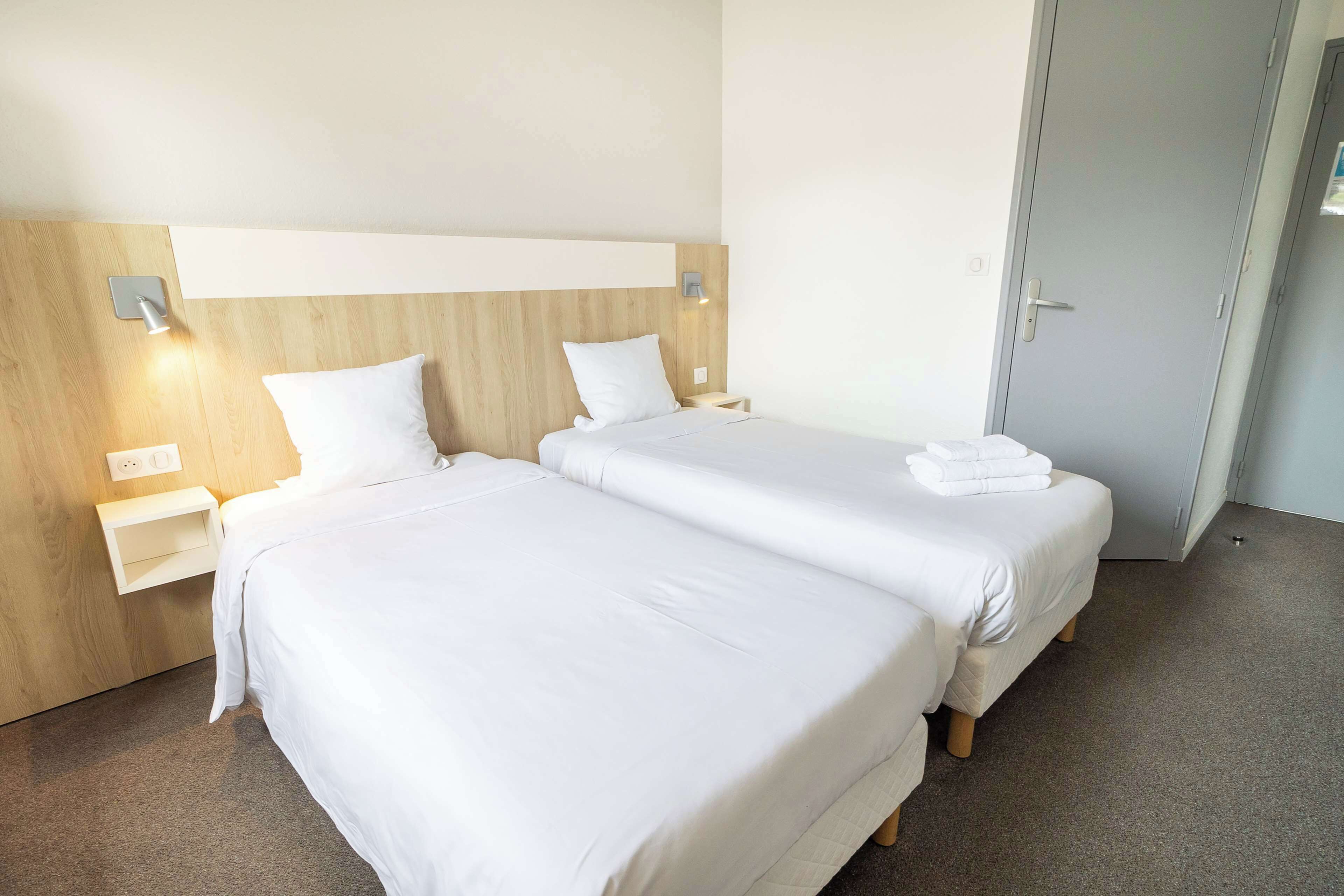 A hotel room with two beds, wooden headboards, bedside tables, and a door.