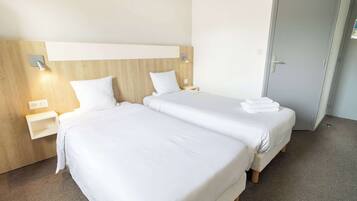 A hotel room with two beds, wooden headboards, bedside tables, and a door.