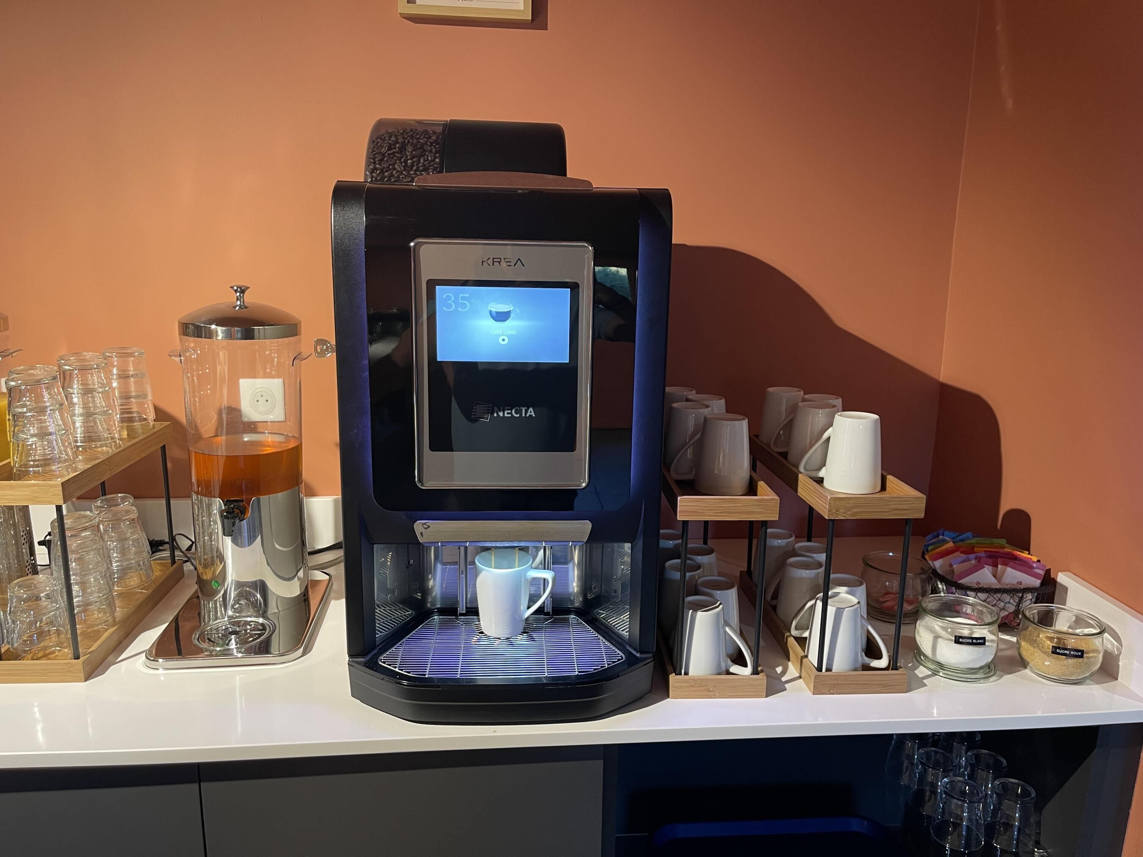 Eine Kaffeemaschine mit digitaler Anzeige, Kaffeetassen sowie Zucker- und Sahnespendern auf einer Theke.