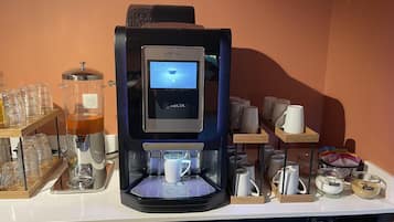 Una máquina de café con pantalla digital, tazas de café y dispensadores de azúcar y leche en una encimera.