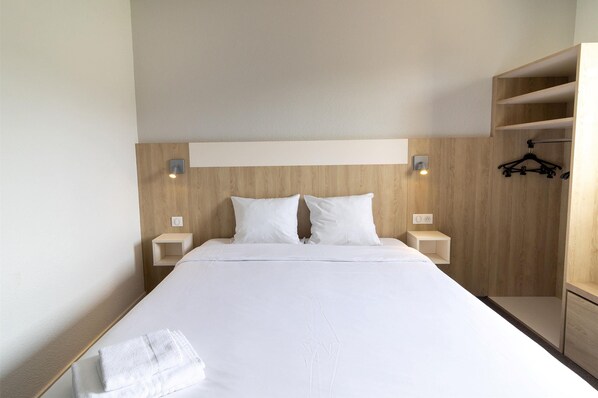 Una cama bien hecha con sábanas blancas, dos mesitas de noche con lámparas y un cabecero de madera.