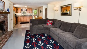 A living room with a gray sectional sofa, a red and white patterned rug, and a brick fireplace. - SPACIOUS & PRIVATE 6 BEDRM HOME CLOSE TO THE OCEAN & BIKE PATH! (Eastham)
