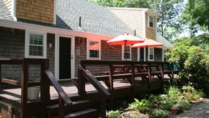 A wooden deck with outdoor seating and a covered area with red umbrellas. - SPACIOUS & PRIVATE 6 BEDRM HOME CLOSE TO THE OCEAN & BIKE PATH! (Eastham)