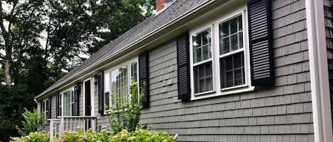 A two-story house with a grey siding exterior, black shutters, and a front porch with a small garden.