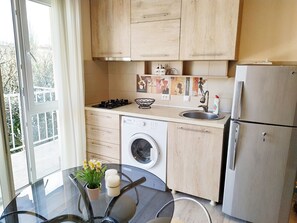 A modern kitchen with wooden cabinets, a built-in washing machine, a stainless steel sink, and a glass dining table with a vase of flowers. - City center - Mariami (Kutaisi)