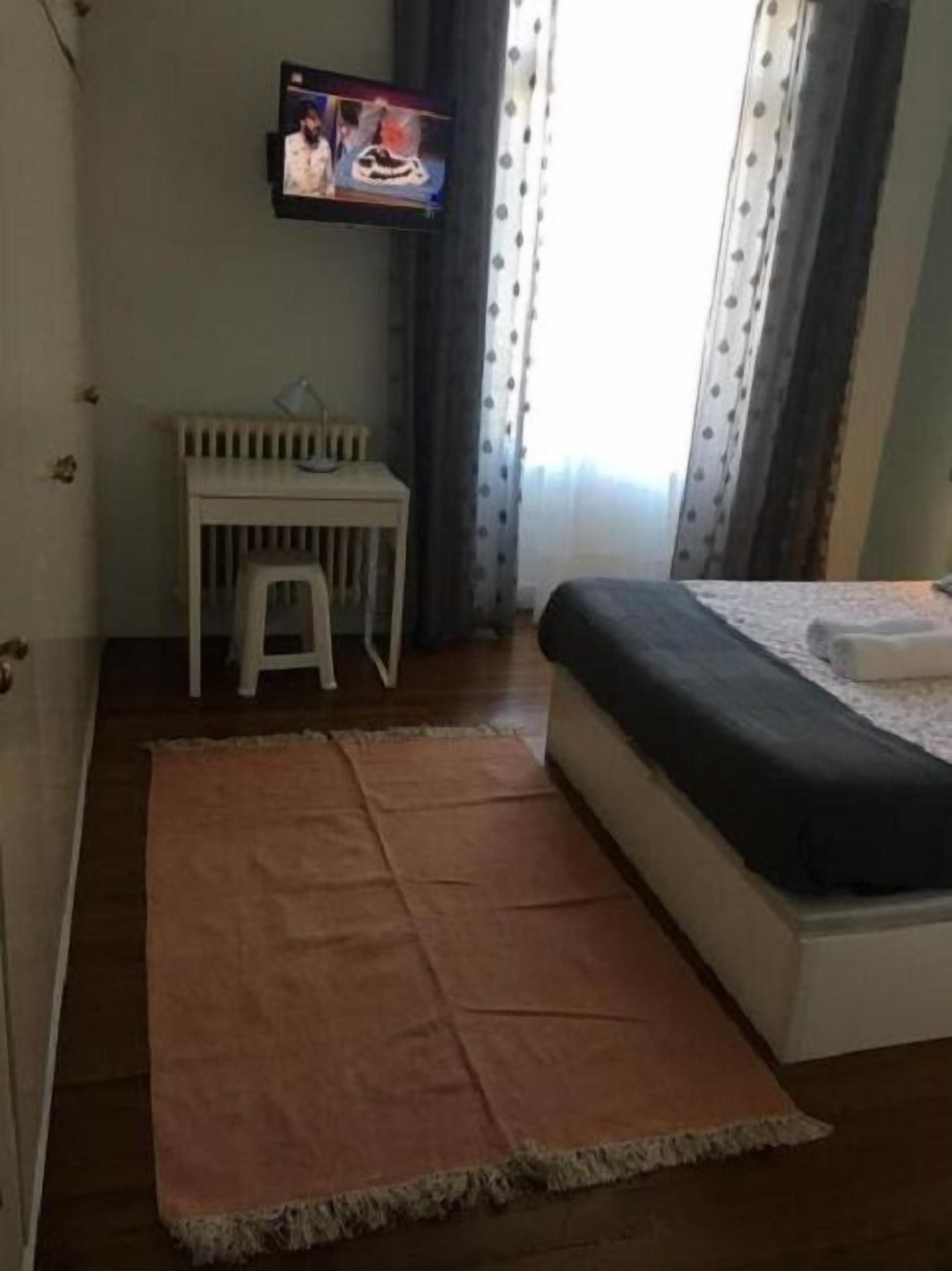 Une petite pièce avec un lit, un téléviseur fixé au mur, une petite table blanche et un tapis.