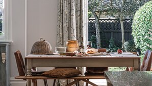 Une table à manger dressée avec des assiettes, un panier en osier, un vase et une bouteille de vin, entourée de chaises.