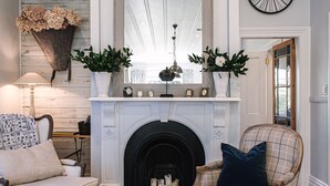 Un salon chaleureux avec une cheminée, deux fauteuils, une table basse avec des livres et un tapis à motifs.