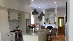 Une cuisine moderne avec des meubles blancs, un îlot central, des luminaires suspendus et un coin repas comprenant une table et des chaises en bois.