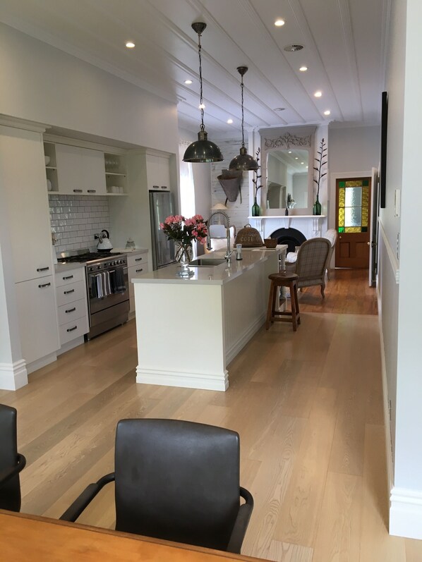Une cuisine moderne avec des meubles blancs, un îlot central, des luminaires suspendus et un coin repas comprenant une table et des chaises en bois.