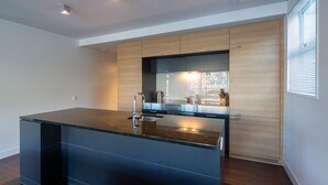 A modern kitchen with a central island, built-in appliances, and a large window. - Marina 2 Bdrm Apartment with Views (Frankton)